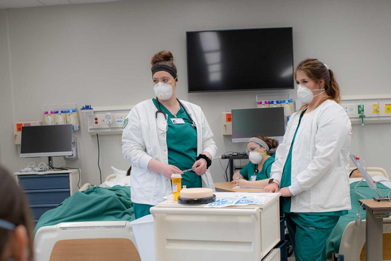 Two nursing students at a medical cart in front of two patient beds